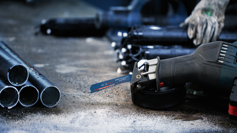 Person wearing safety equipment uses a reciprocating saw to cut a metal pipe.