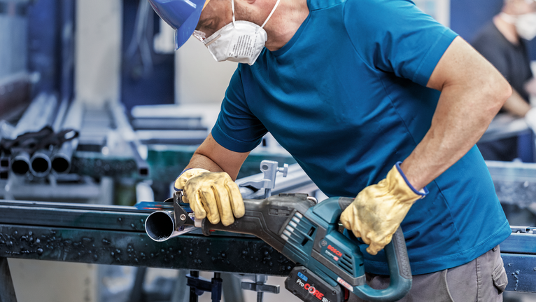 Person wearing safety equipment uses a reciprocating saw to cut a metal pipe.