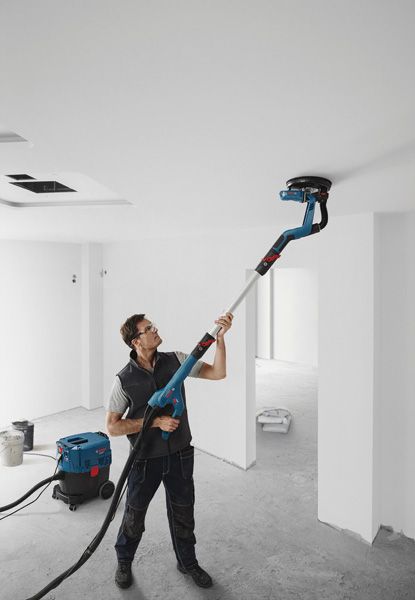 GTR 55-225 A person wearing safety equipment sands a ceiling with a drywall sander in an unfinished room.
