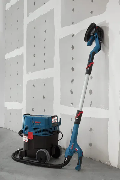 GTR 55-225 Drywall sander connected to a dust extractor standing against an unfinished wall.