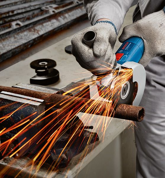 A person wearing safety equipment grinds a metal pipe with an angle grinder.