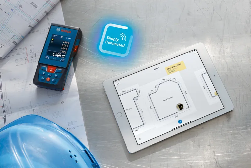 GLM 100-25 C Laser measure next to blueprints and tablet displaying a digital floor plan.