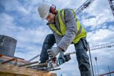 A person wearing safety equipment grinds rebar with a power tool at a construction site.