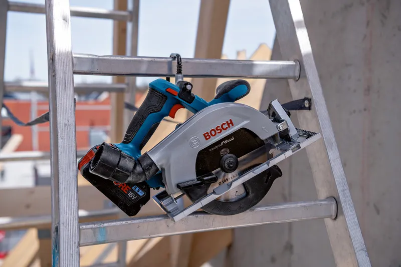 Cordless circular saw resting on a metal ladder at a construction site.