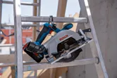 Cordless circular saw resting on a metal ladder at a construction site.