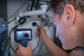 Person using an inspection camera to examine plumbing under a sink.