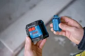 Person holds a blue laser leveling tool and its battery compartment indoors.