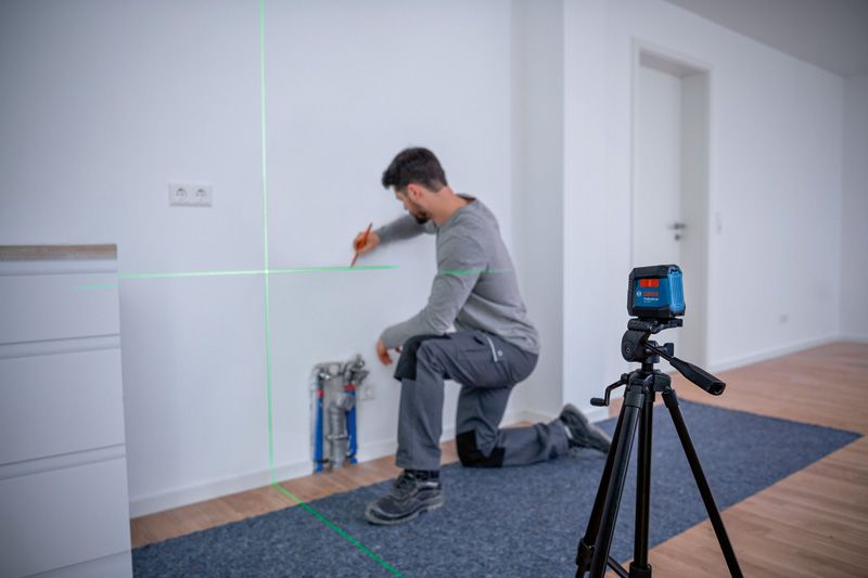 A person marks a wall using a laser leveling tool set on a tripod.