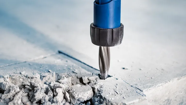 A rotary drill bit makes a hole in a concrete surface.