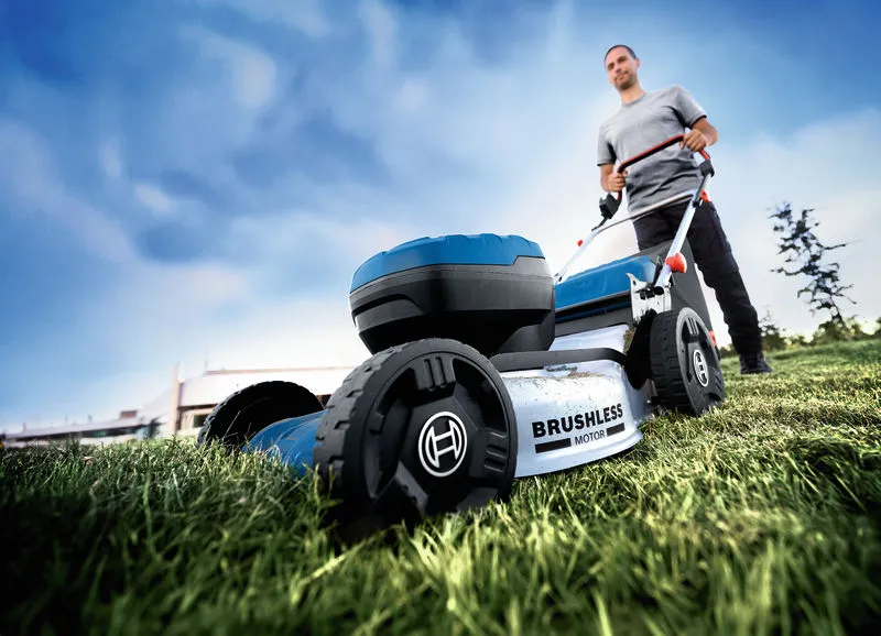 GRA 18V2-46 A person pushes a cordless lawnmower over grass in an outdoor area.