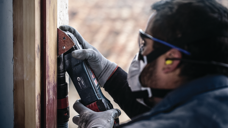 PRO F460 Sanding Sheet, 93 x 93 mm, G40, 5 pcs Person wearing safety equipment sands a wooden frame using a power tool.