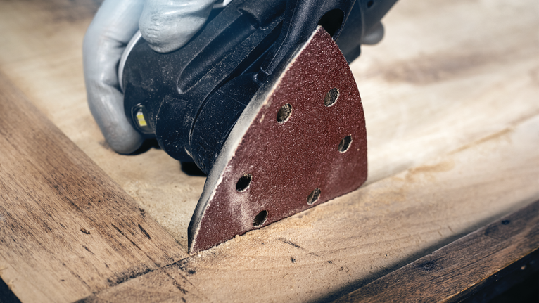 PRO F460 Sanding Sheet, 93 x 93 mm, G40, 5 pcs Person wearing safety equipment sands a wooden surface with a detail sander.