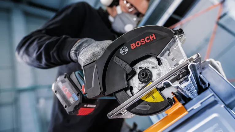 A person wearing safety equipment uses a circular saw to cut metal.