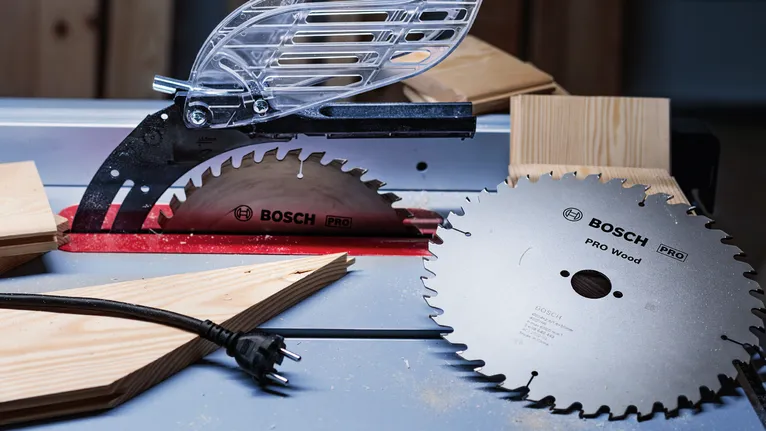 PRO Wood Circular Saw Blade, 216 x 2.6 x 30 mm, T34 Circular saw blades and wooden planks placed on a workbench in a workshop.