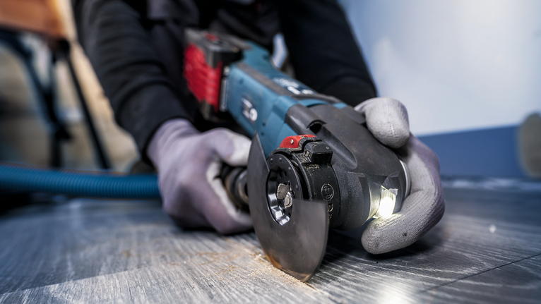 Person wearing safety equipment uses an angle grinder to cut a tile floor.