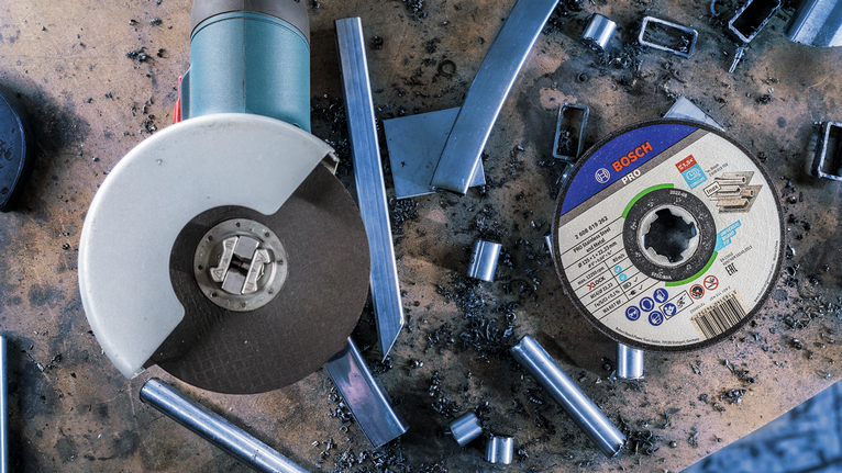PRO Stainless Steel and Metal Bonded Cutting Disc, 125 x 1 x 22.23 mm, X-Lock, Straight Angle grinder and metal cutting disc on a workbench with scattered metal scraps.