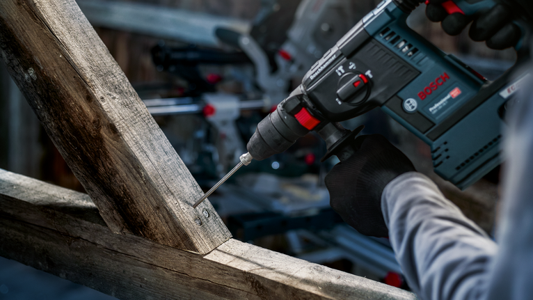 Person wearing safety equipment drills into a wooden beam.