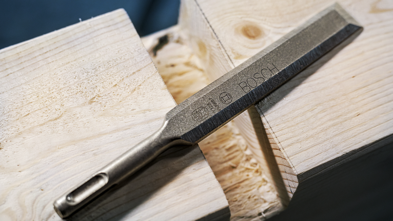 Metal chisel resting on a wooden surface in a workshop.