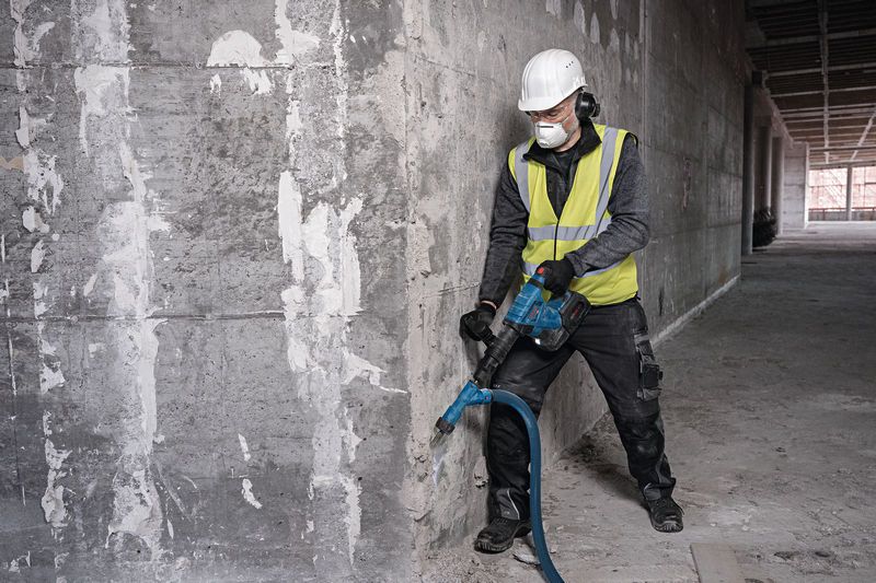 A person wearing safety equipment breaks concrete with a cordless demolition hammer.