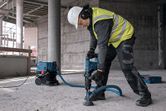A person wearing safety equipment drills concrete with a dust extraction attachment.