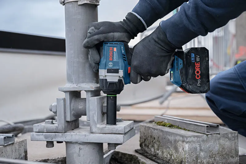 GDS 18V-750 C A person wearing safety equipment fastens a large bolt on a metal structure with a cordless impact wrench.