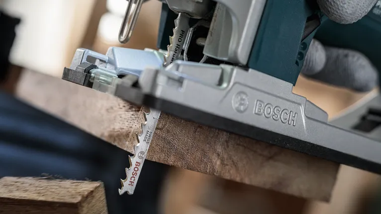 Person wearing safety equipment uses a jigsaw to cut a wooden board.