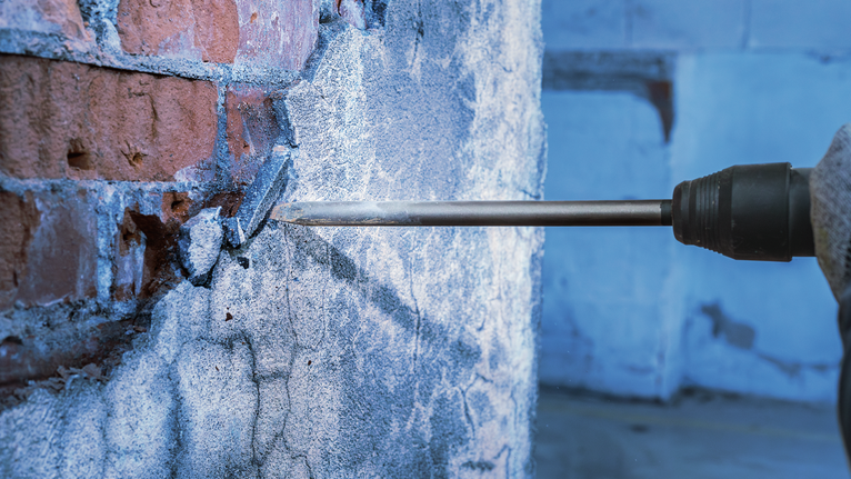 PRO SDS max-4C Pointed Chisel, 300 mm Chisel drill breaking into a brick wall, worker wearing safety equipment.