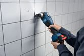 A person cuts into wall tiles using a cordless multi-cutter.