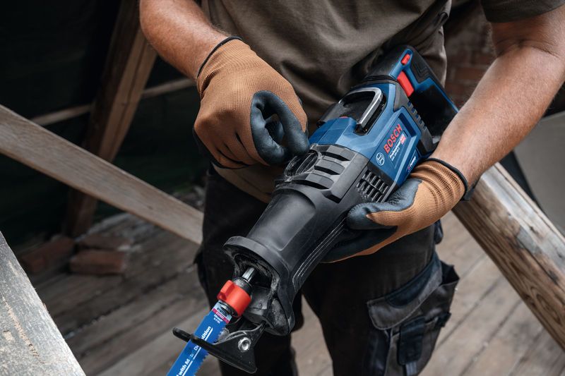A person wearing safety equipment adjusts a reciprocating saw at a construction site.