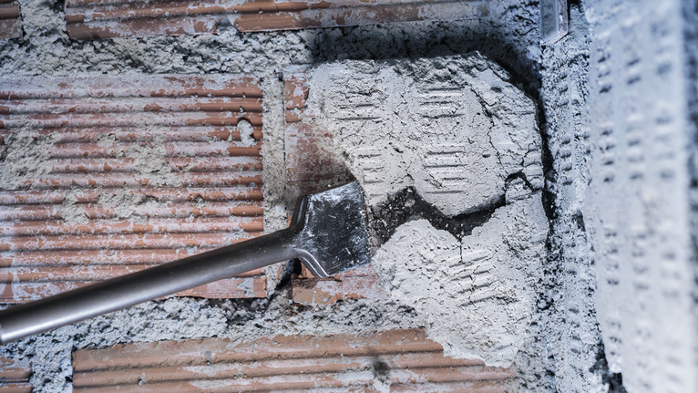Chisel breaking concrete on a brick wall surface.
