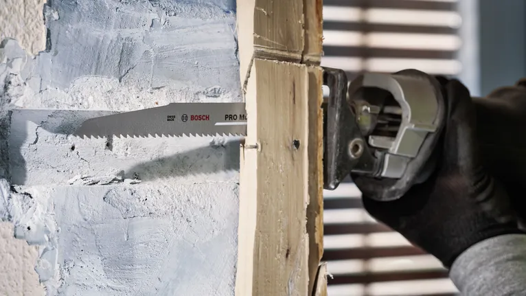 Person wearing safety equipment cuts through a wooden stud using a reciprocating saw.
