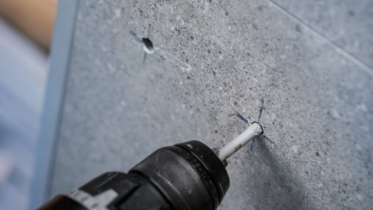 Drill making a precise hole in a grey tiled surface.