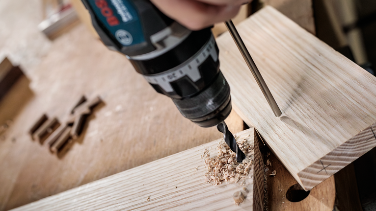PRO Wood Brad Point Drill Bit, 18 x 130 x 180 mm Person drills a hole into wooden boards in a workshop.
