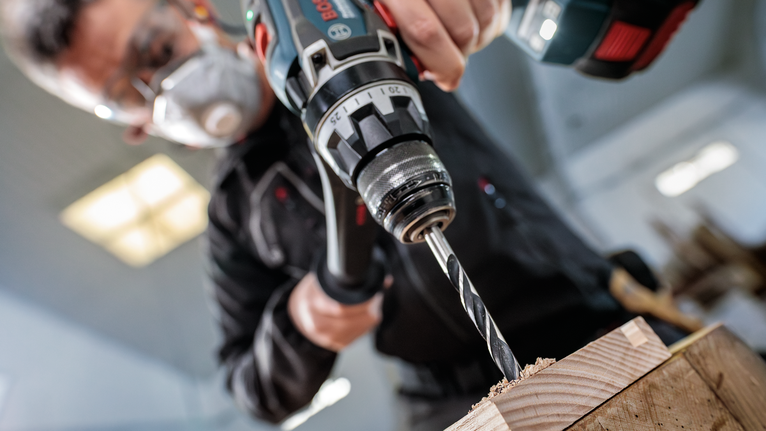 PRO Wood Brad Point Drill Bit, 18 x 130 x 180 mm A person wearing safety equipment drills into wood.