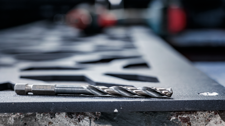 PRO Metal HSS-G Impact Twist Drill Bit Set, 8 pcs Metal drill bit resting on a cut steel sheet in a workshop.