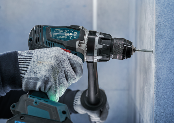 Person wearing safety equipment drills a screw into a wall.