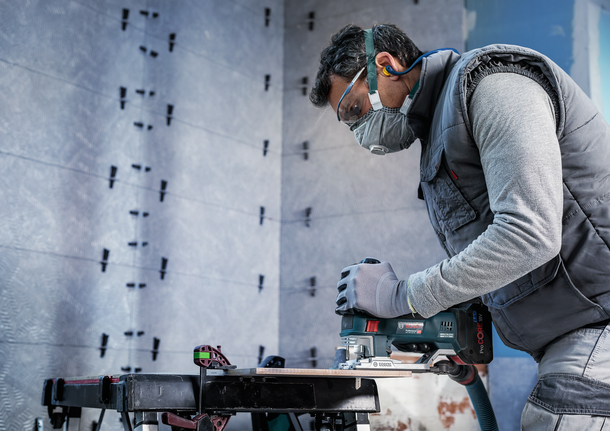 PRO Soft Tile T130RF Jigsaw Blade, 83 mm, 3 pcs A person wearing safety equipment uses a jigsaw to cut wood on a workbench.