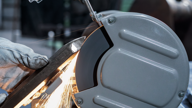 PRO Metal Grinding Wheel, 200 x 25 x 32 mm, G60 A person wearing safety equipment grinds a metal bar with a bench grinder.