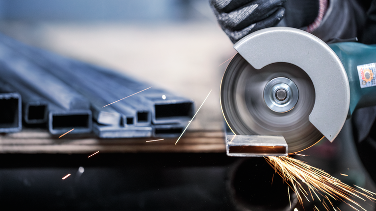 PRO Stainless Steel and Metal Cutting Disc, 105 x 1 x 16 mm A person wearing safety equipment cuts a metal pipe with a circular saw, sparks flying.