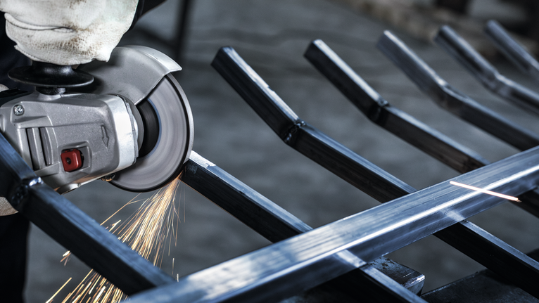 Person wearing safety equipment uses an angle grinder to cut metal, creating sparks.