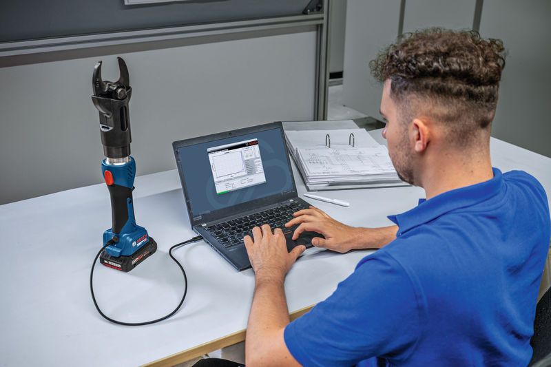 A person connects a cordless hydraulic cutting tool to a laptop for data analysis.