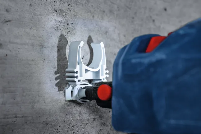 Rotary hammer drills into concrete to install a white mounting bracket.