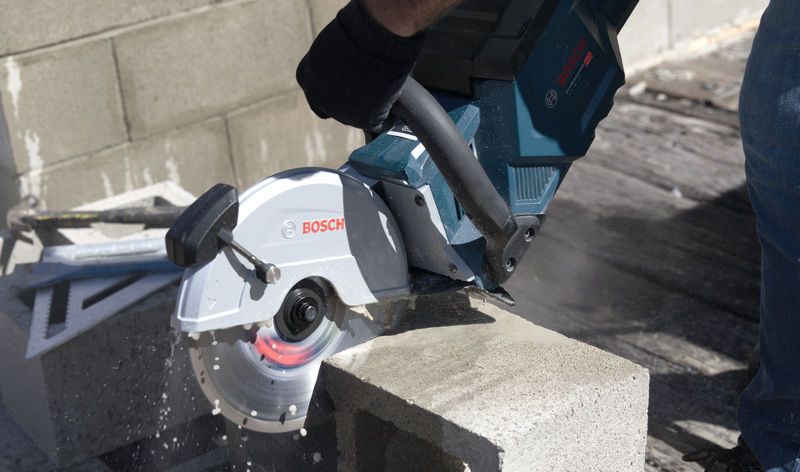 A person wearing safety equipment cuts a concrete block with a cordless grinding saw.