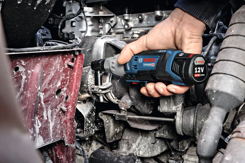 A person uses a cordless ratchet wrench to fasten a bolt in an engine compartment.