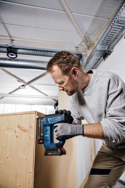 GNH 18V-35 Person wearing safety equipment uses a jigsaw to cut wood in a workshop.
