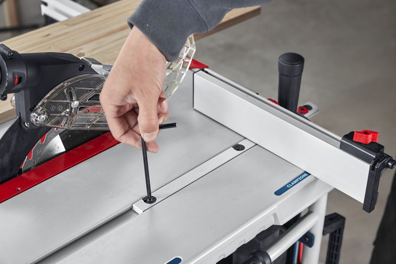 Person adjusts a table saw with an Allen key near a mounted guide rail.