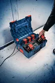 A person places a battery into a blue multi-battery charger case on a concrete floor.