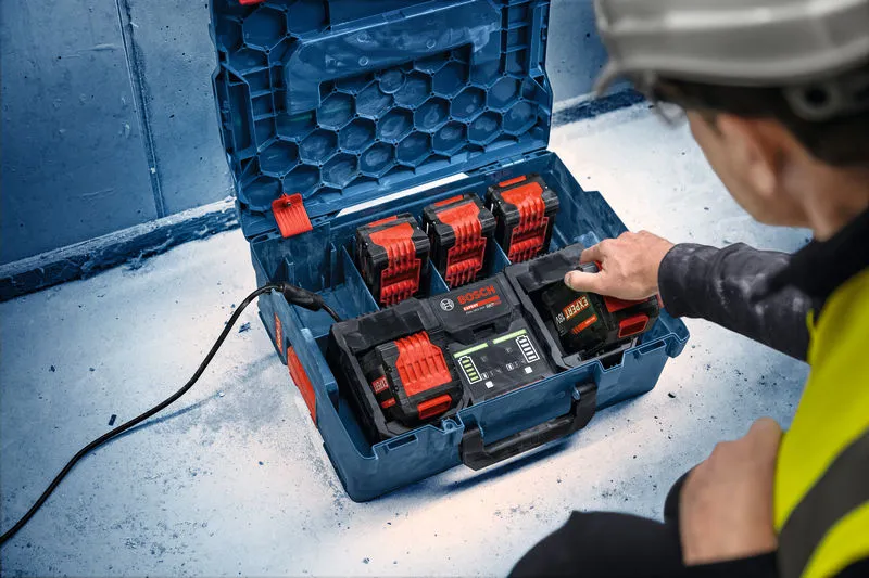 A person wearing safety equipment operates a multi-battery charging station on a job site.