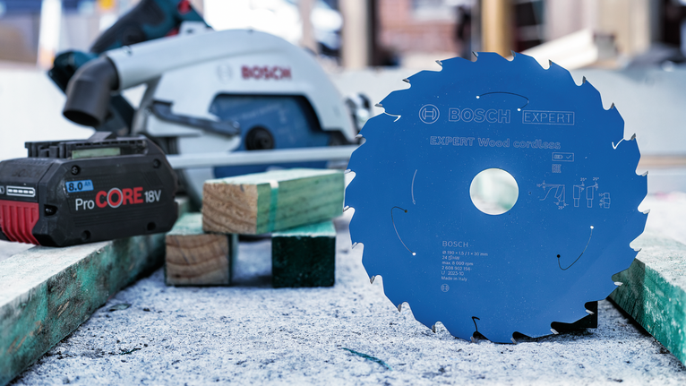 Circular saw blade stands upright on a workbench beside a cordless battery and saw.