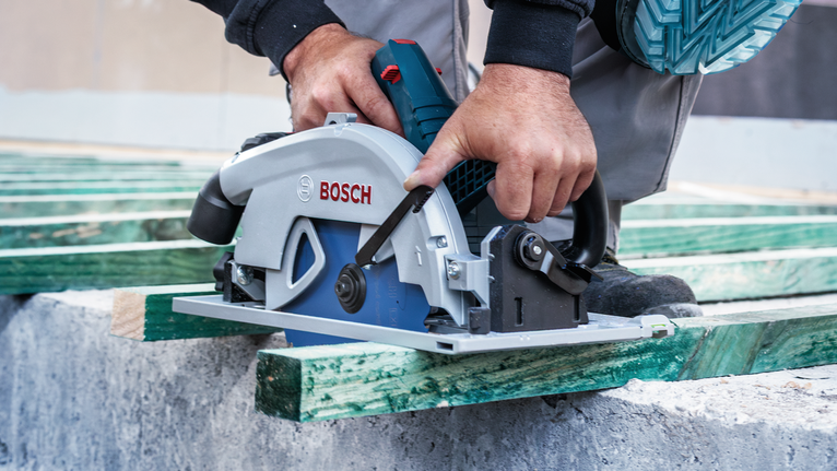 Person wearing safety equipment operates a circular saw to cut green wooden beams.